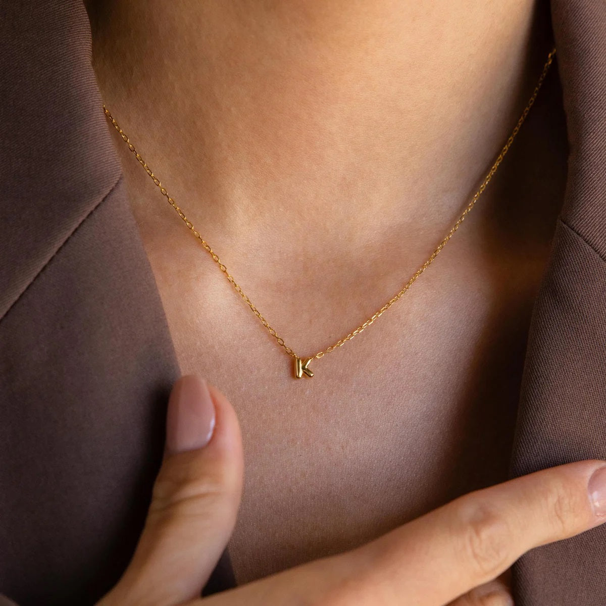 Gold necklace with a 'K' pendant on a person wearing a brown garment.