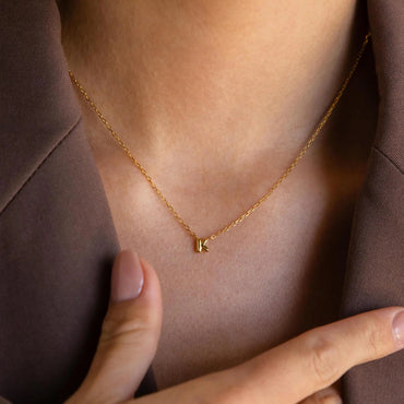 Gold necklace with a 'K' pendant on a person wearing a brown garment.