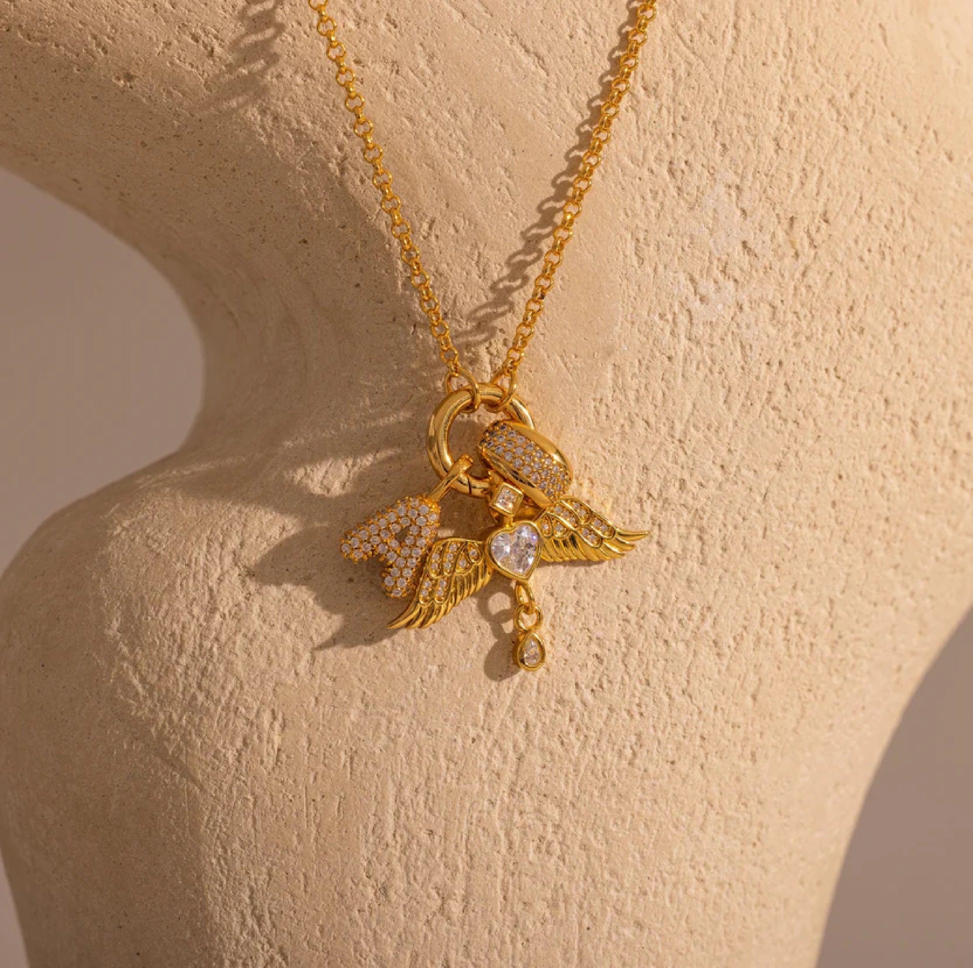 Gold necklace with heart and leaf pendant on a beige surface