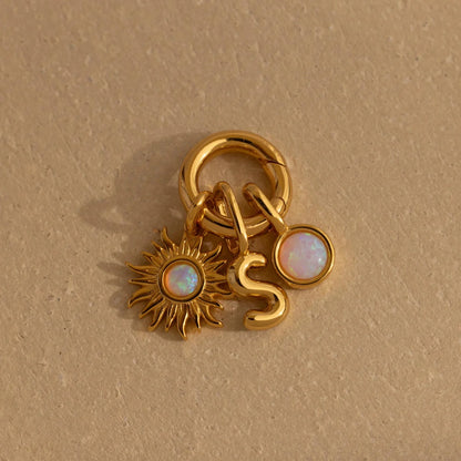 Gold charm with sun design and 'S' letter on a beige background