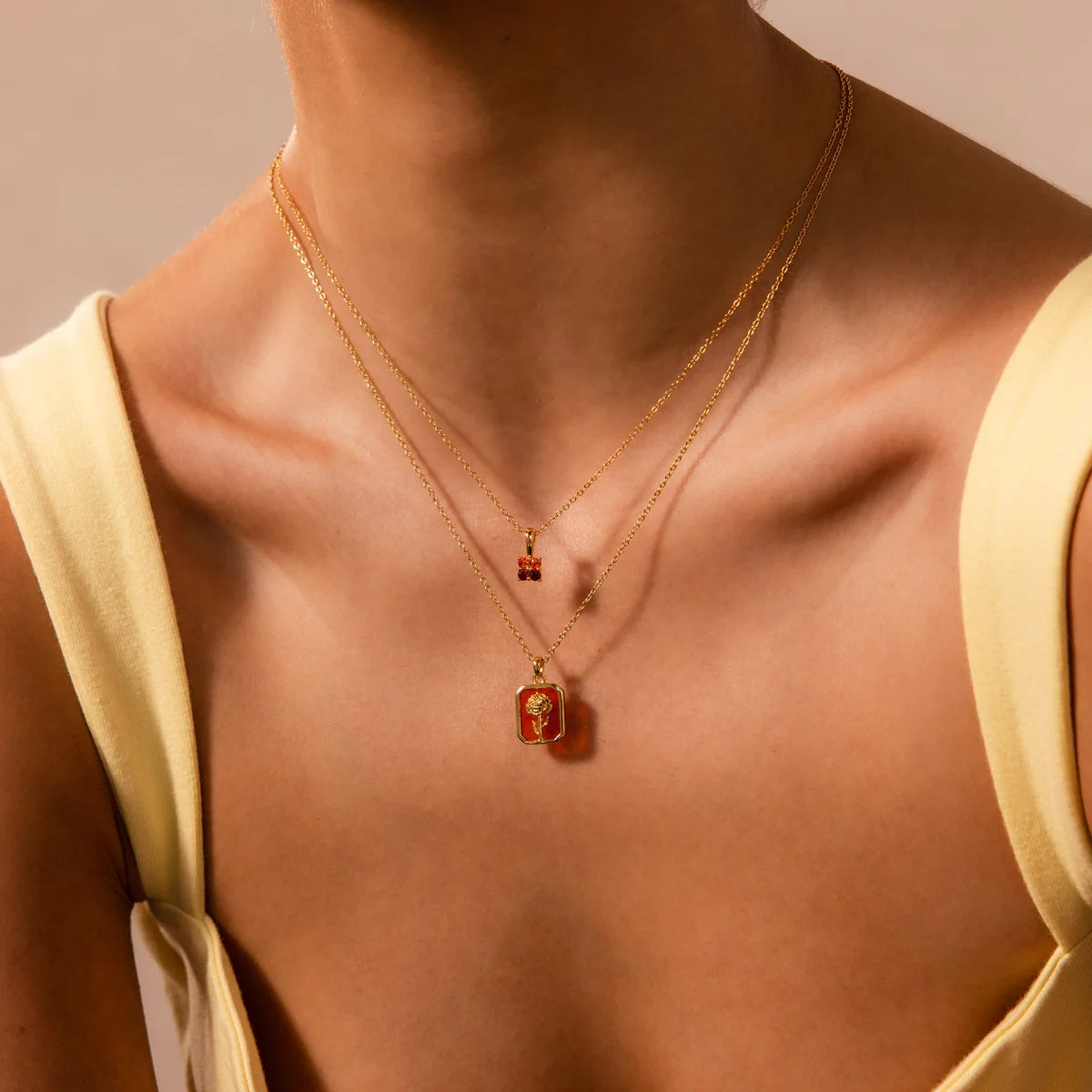 Close-up of a person wearing two gold necklaces with pendants on a beige background