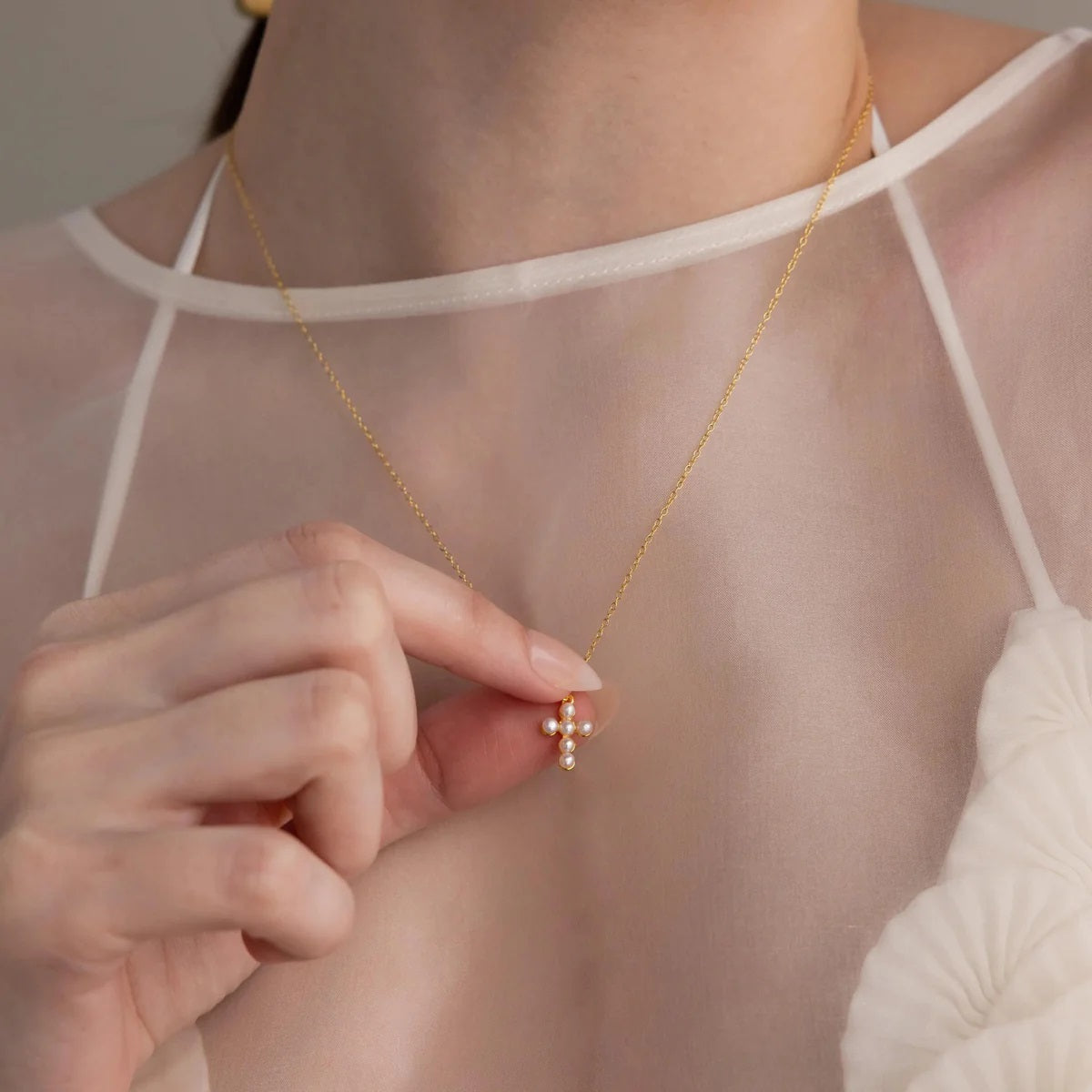 Gold necklace with a small pendant worn by a person in a sheer top.
