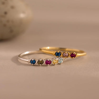Two rings, one silver and one gold, with colorful gemstones on a beige background.