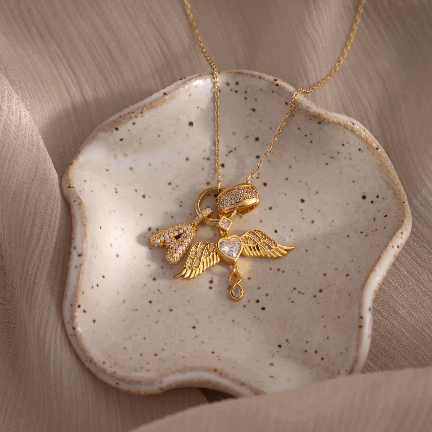 Gold necklace with heart and wing pendant on a ceramic dish