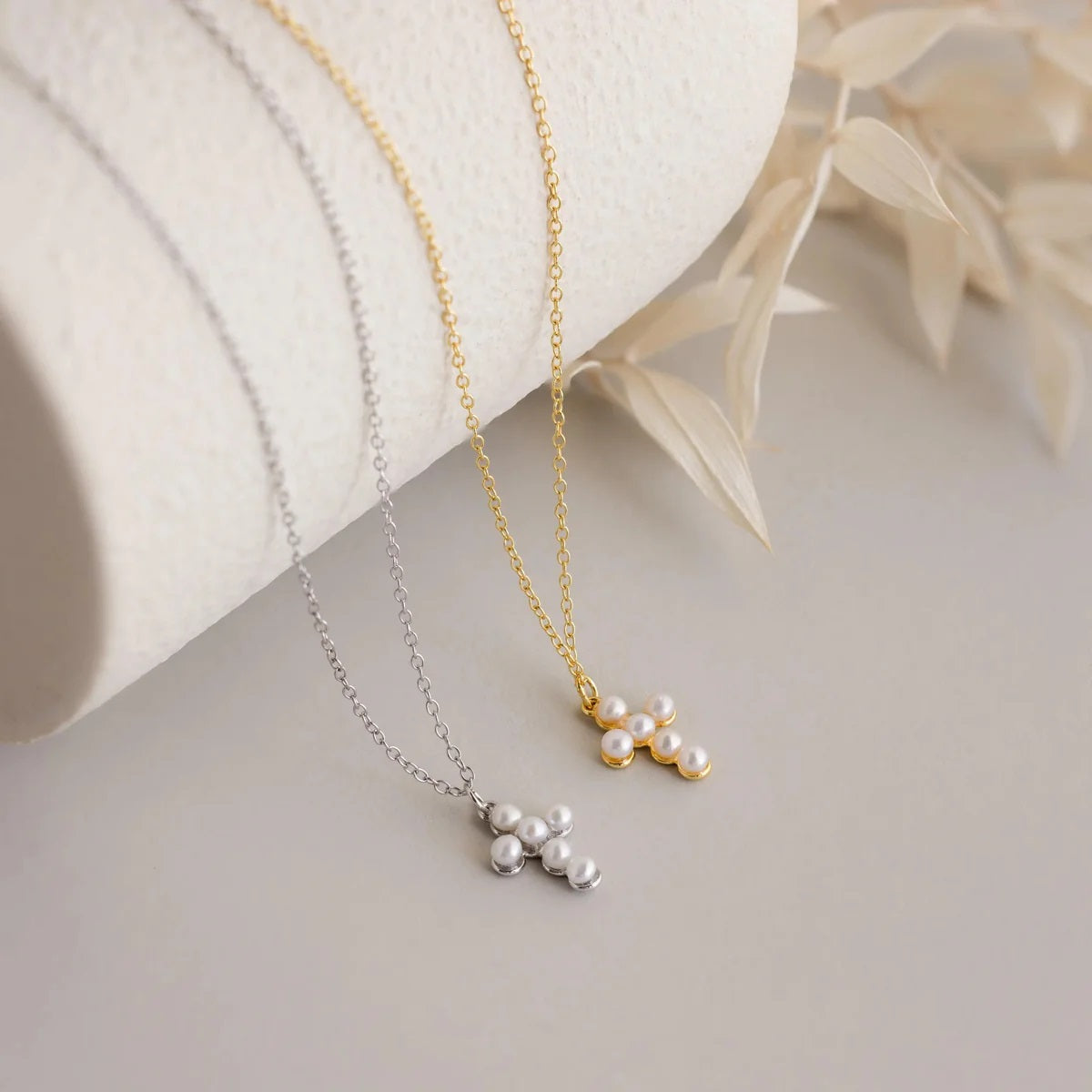 Two pearl necklaces, one gold and one silver, on a light surface with a white fabric background.