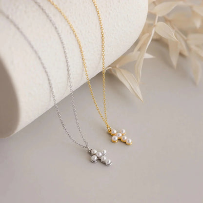 Two pearl necklaces, one gold and one silver, on a light surface with a white fabric background.