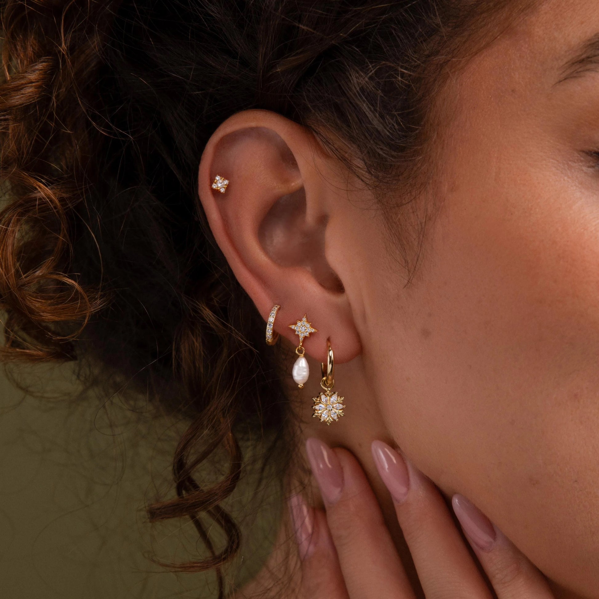 Close-up of an ear with multiple diamond earrings and a hand adjusting them.