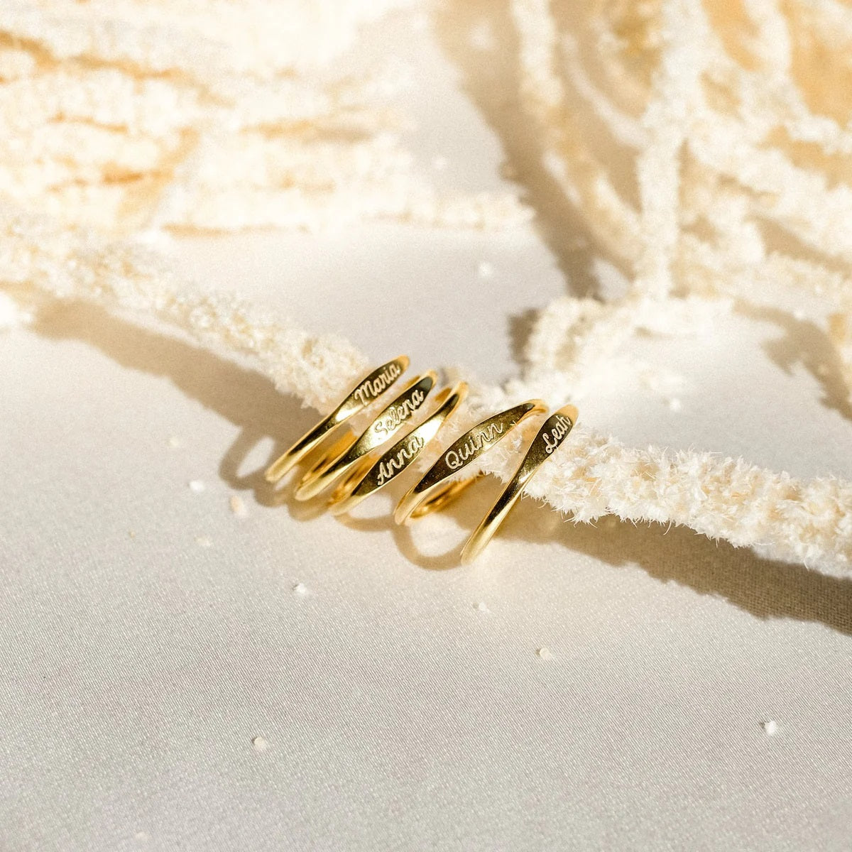 Gold rings with engraved names on a textured beige surface