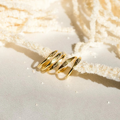 Gold rings with engraved names on a textured beige surface