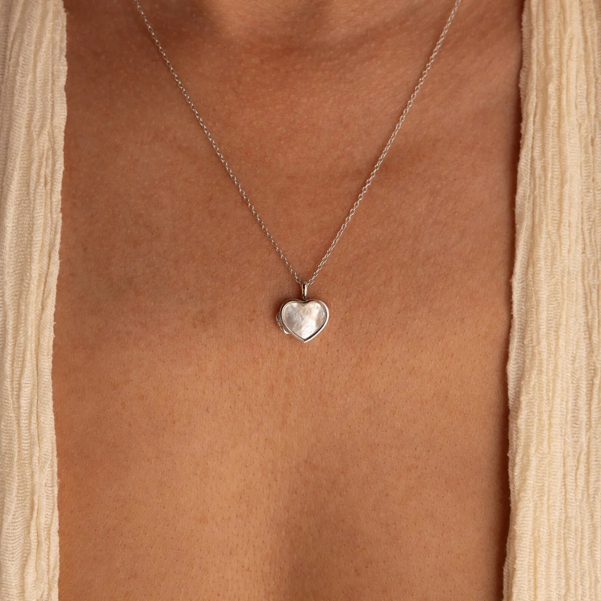 Heart-shaped silver pendant necklace on a person wearing a beige top.