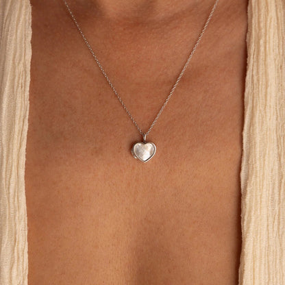 Heart-shaped silver pendant necklace on a person wearing a beige top.
