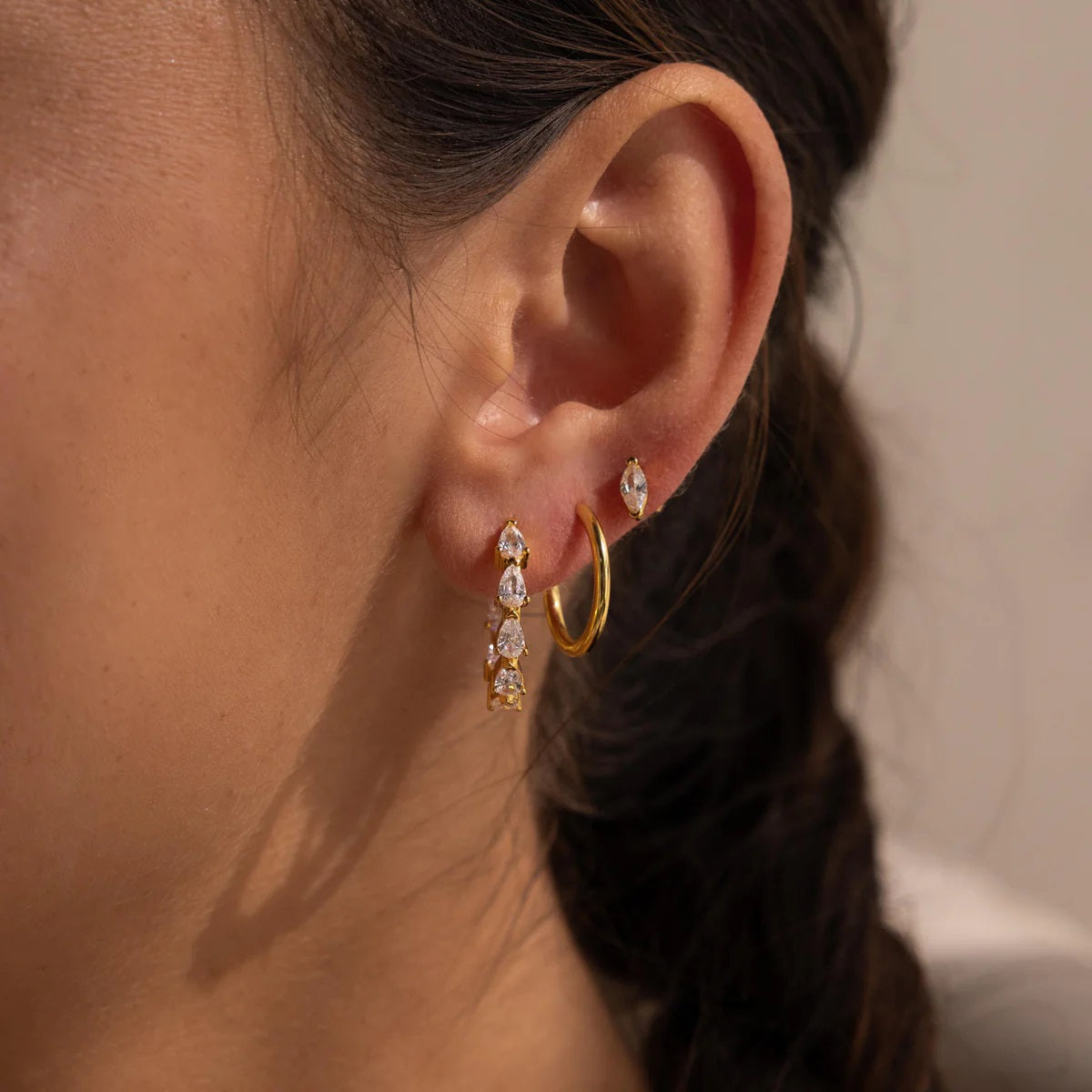 Close-up of an ear wearing gold hoop earrings with clear gemstones.