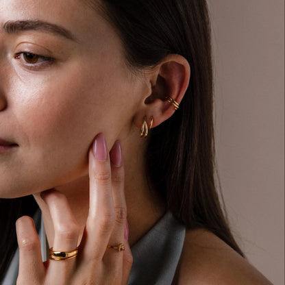 Woman wearing gold earrings and rings on a neutral background