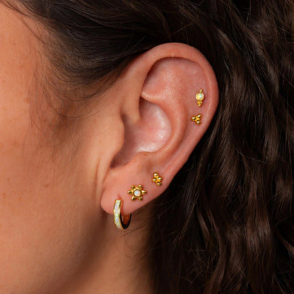 Close-up of an ear wearing gold earrings with a dark background