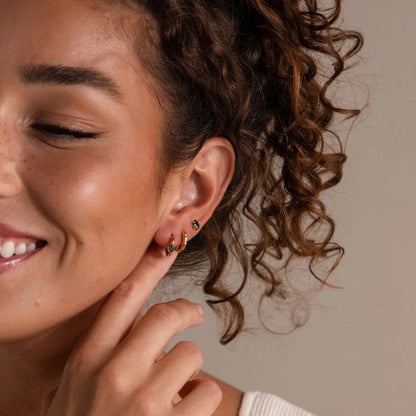 Woman with curly hair wearing earrings, smiling against a neutral background