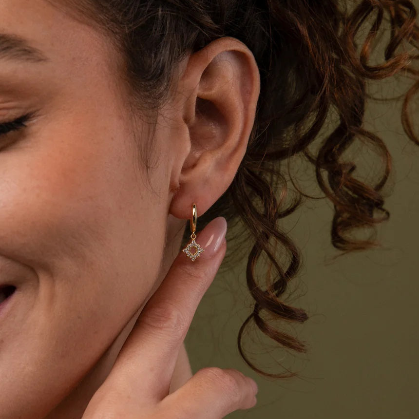 Woman wearing a diamond earring, smiling and touching her ear.