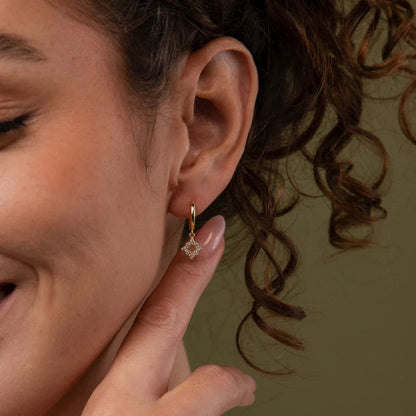 Woman wearing a diamond earring, smiling and touching her ear.