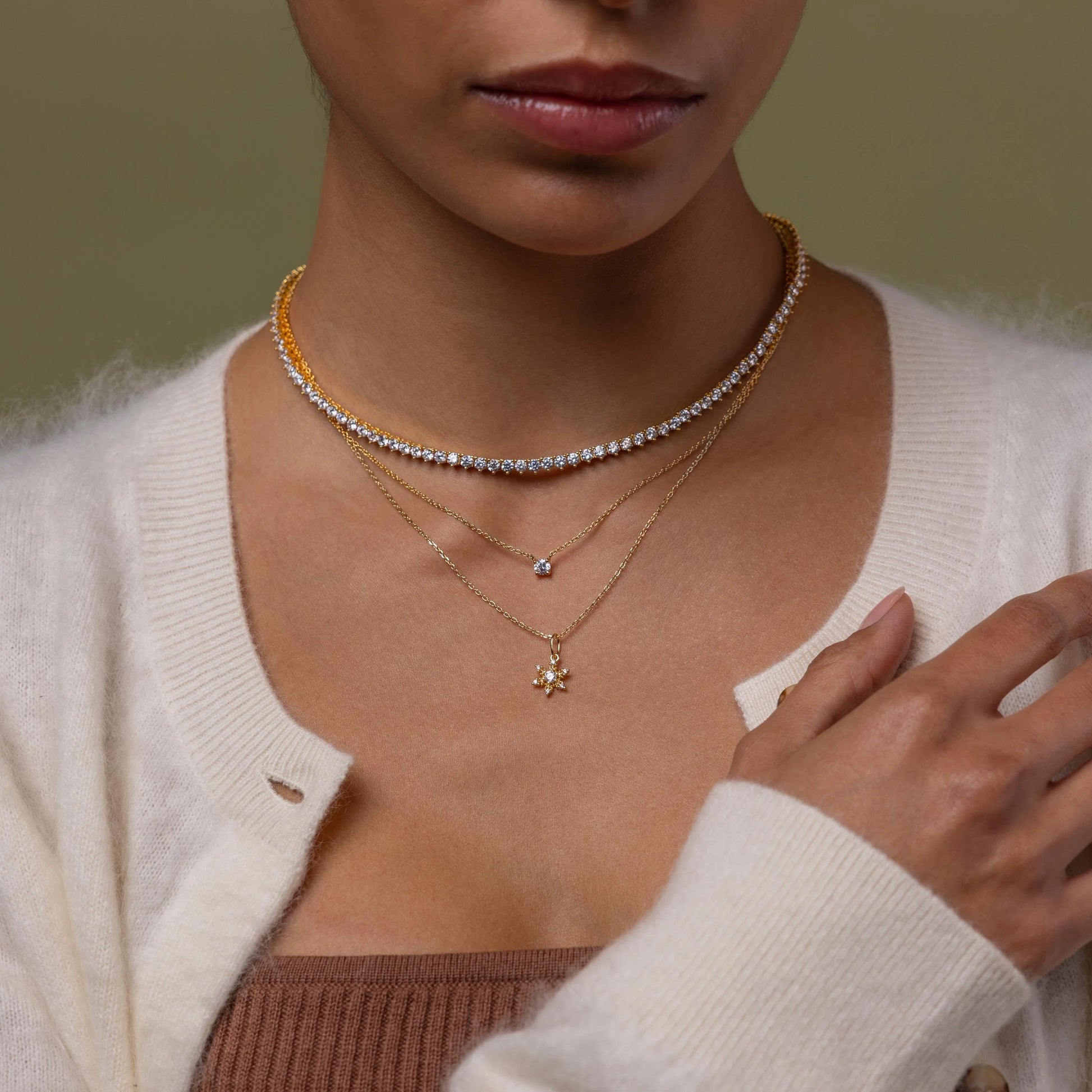 Close-up of a person wearing multiple necklaces with a neutral background