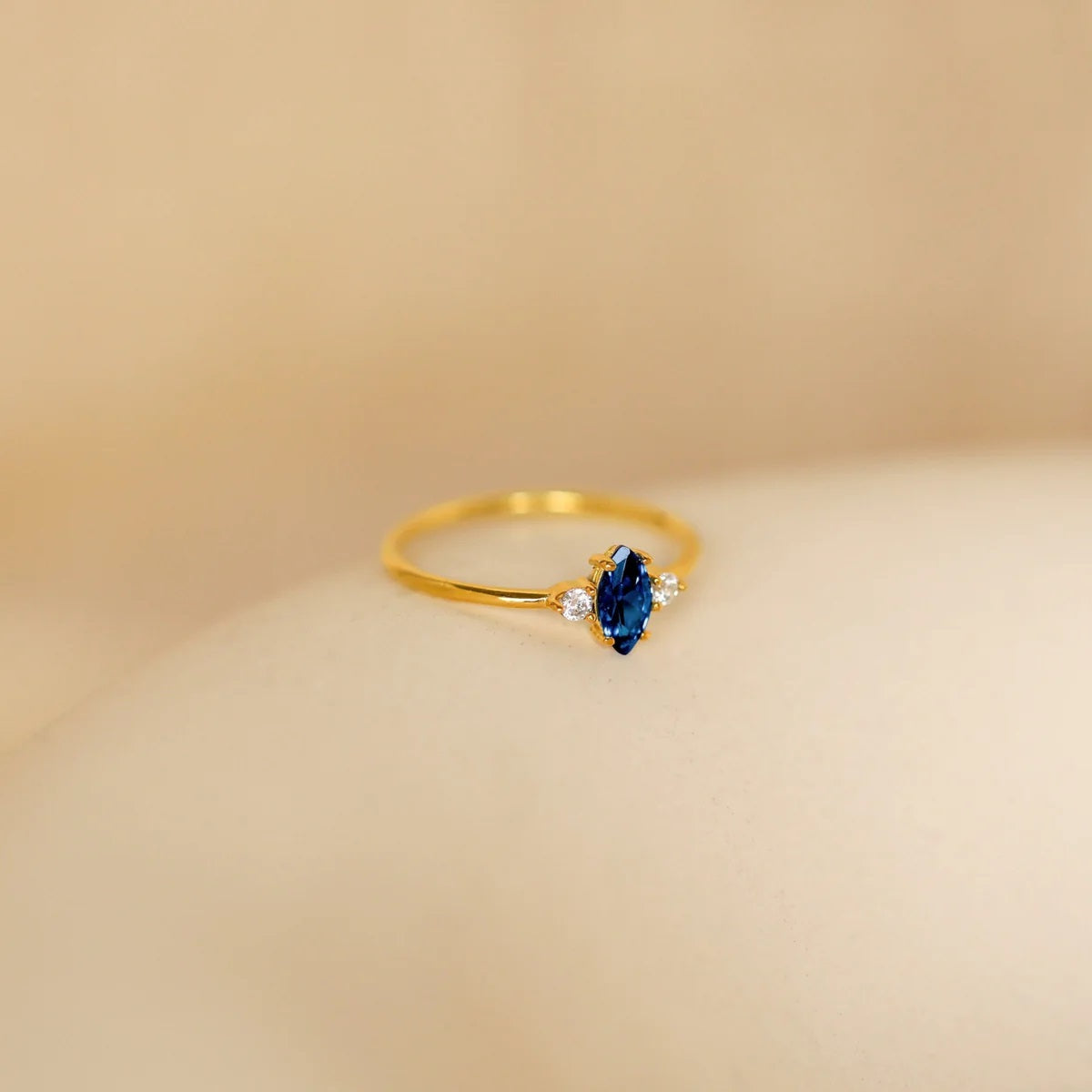 Gold ring with a blue gemstone on a beige background