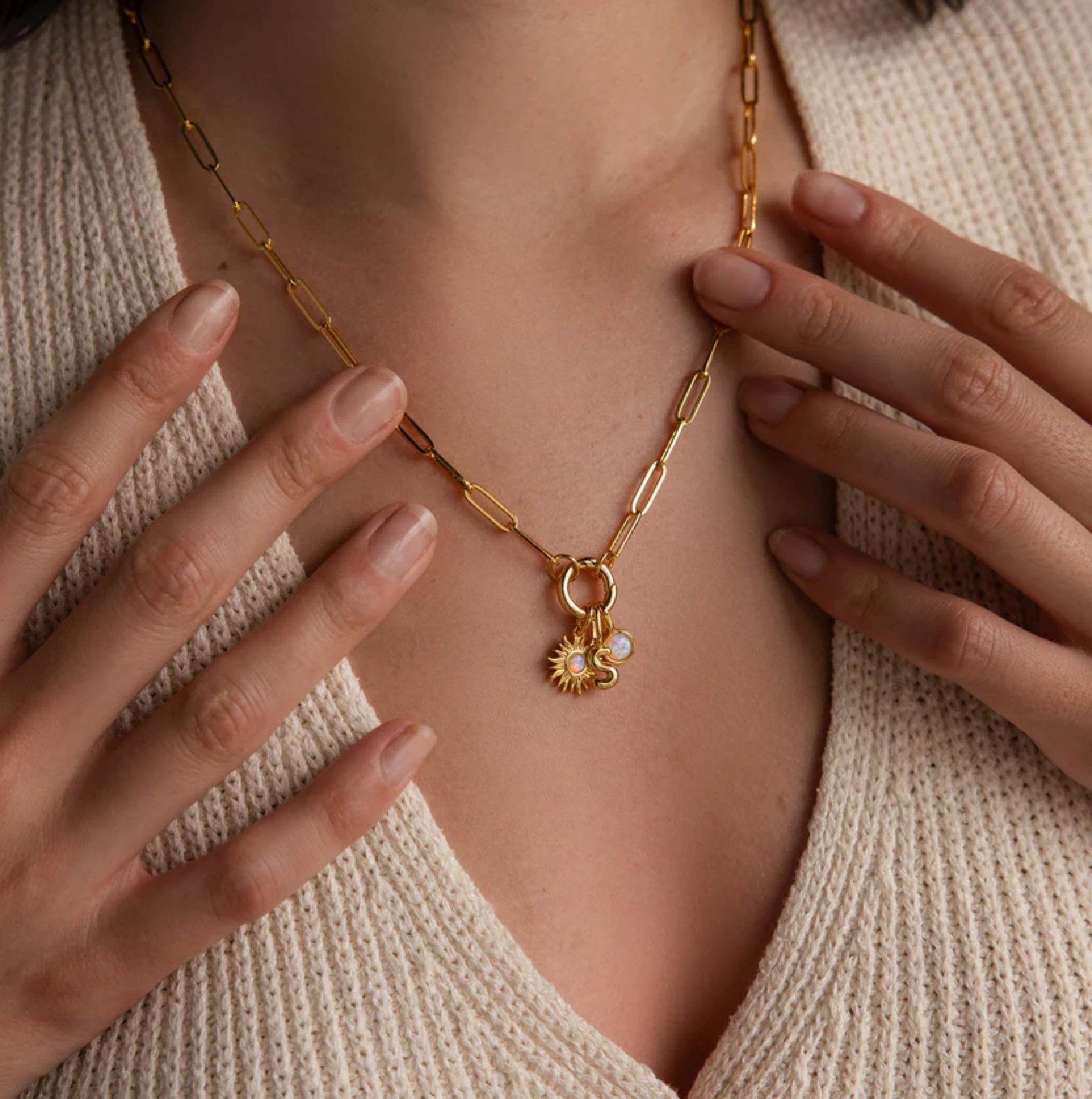 Gold necklace with charms worn by a person, close-up of the necklace and hands.
