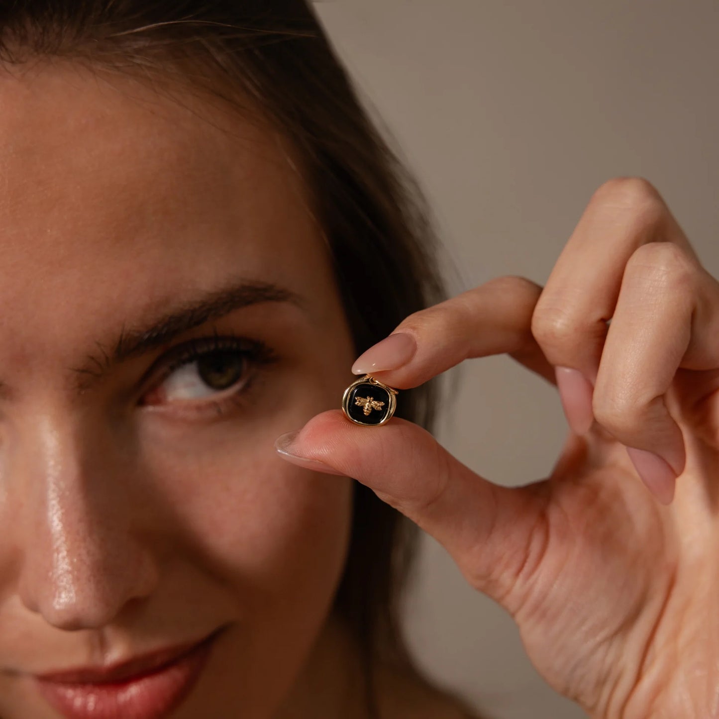 Woman holding a small round object with a bee design close to her face against a neutral background