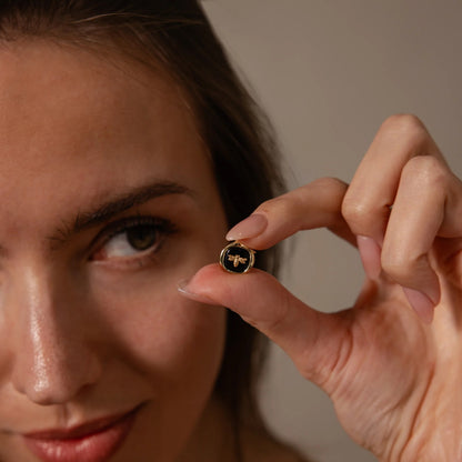 Woman holding a small round object with a bee design close to her face against a neutral background