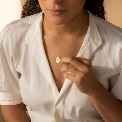Woman wearing a white shirt and gold necklace, holding the necklace with her hand.
