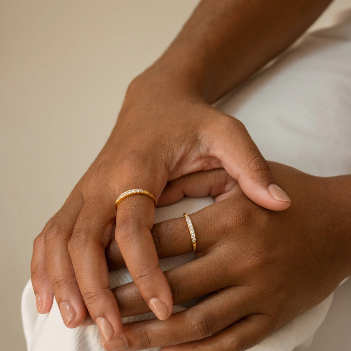 Two hands with gold rings on a neutral background