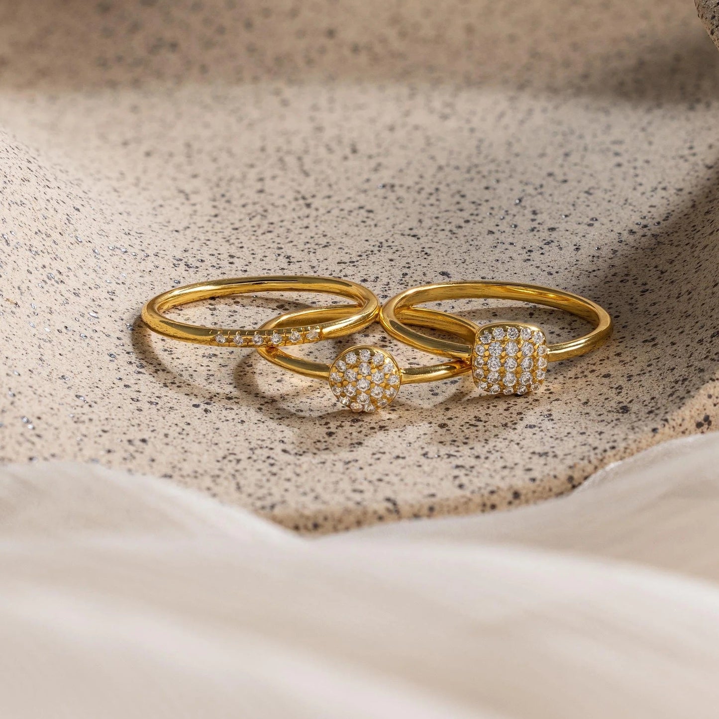 Two gold rings with diamond accents on a textured beige surface