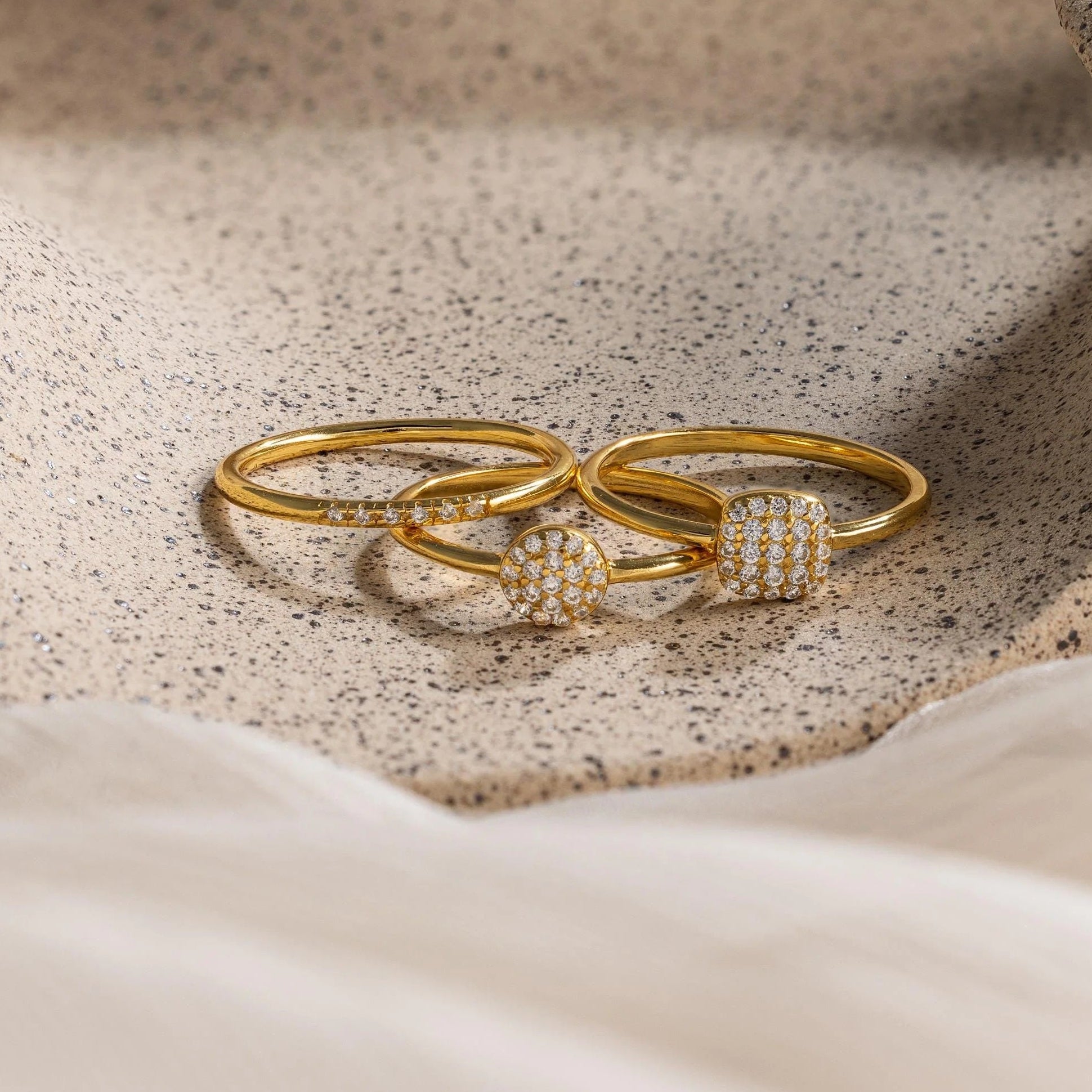Two gold rings with diamond accents on a textured beige surface
