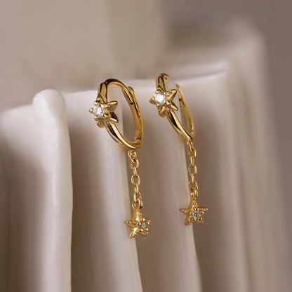 Gold hoop earrings with star-shaped charms on a beige background