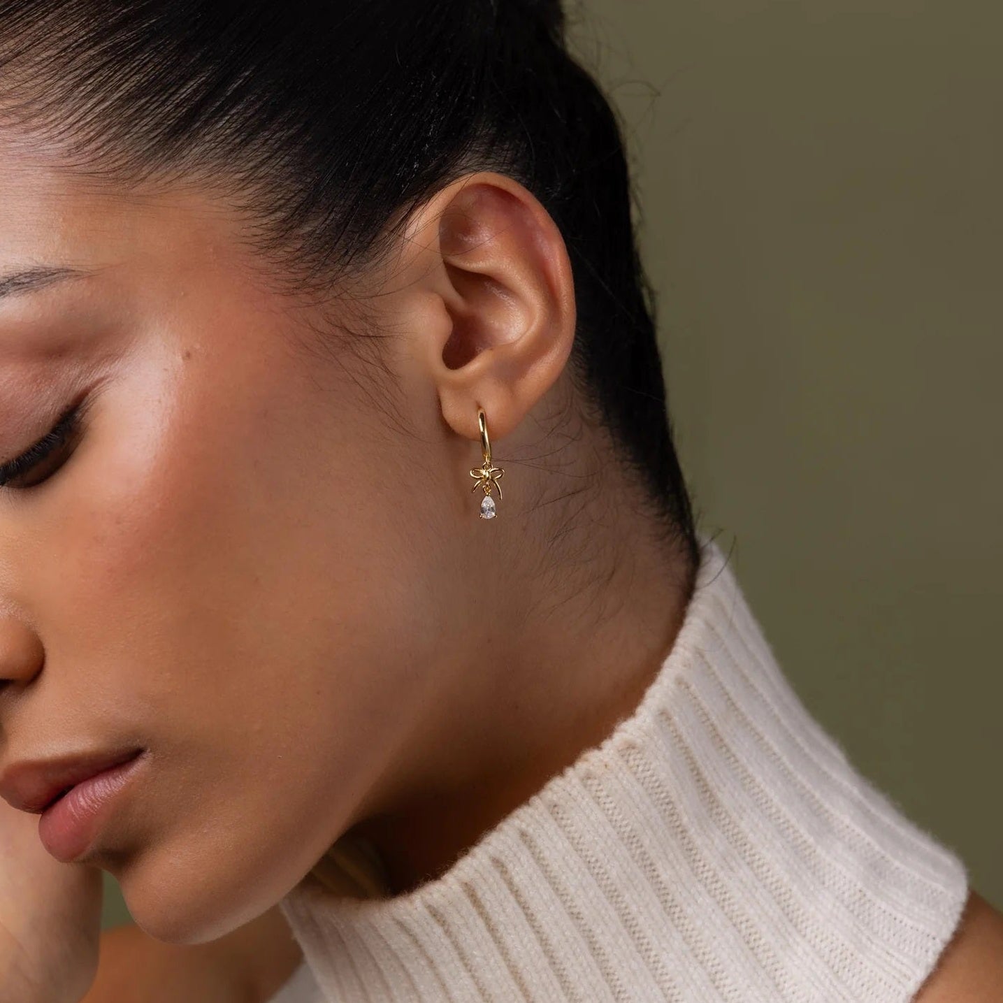 Close-up of a woman wearing a gold earring with a pearl on a neutral background