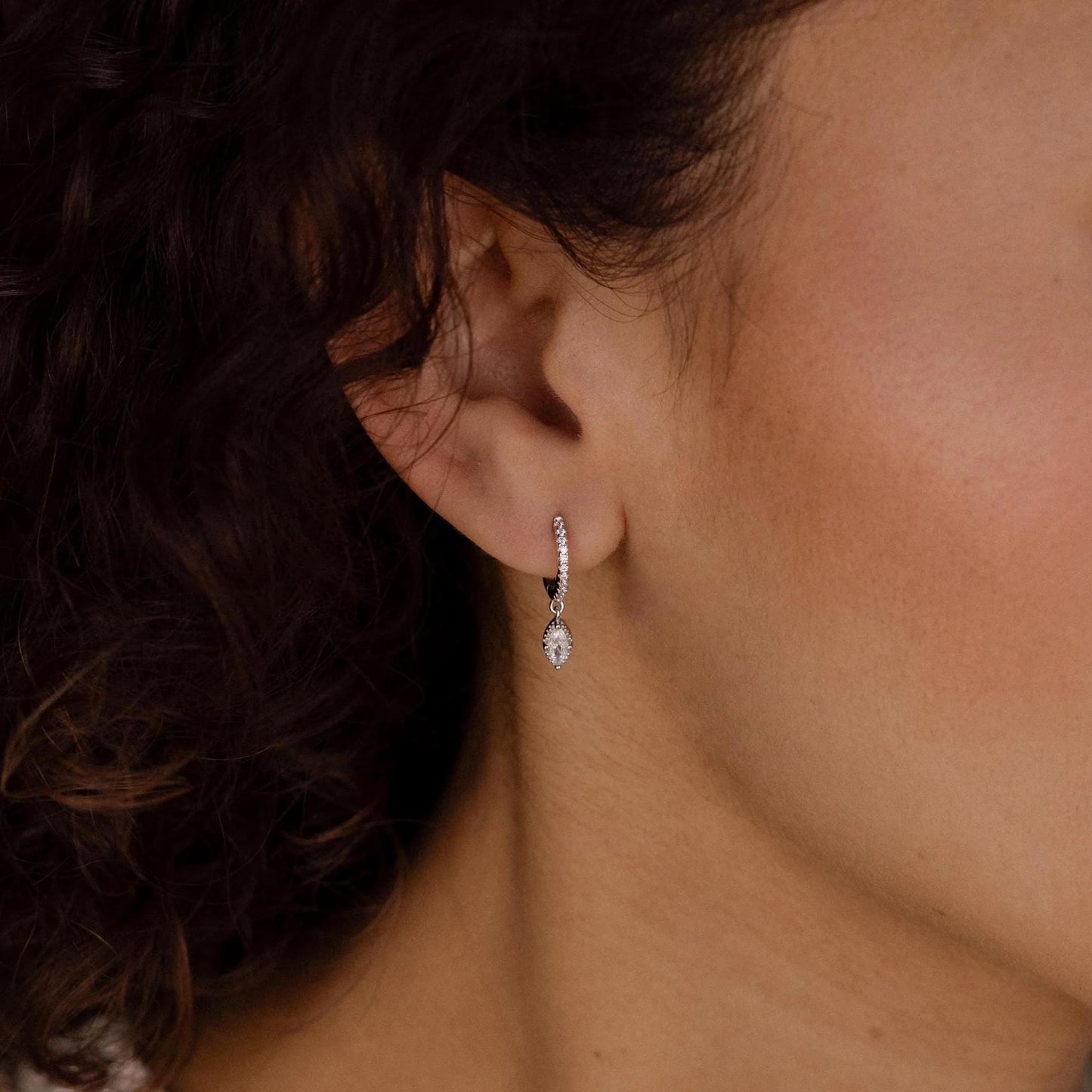 Close-up of an ear wearing a diamond earring with dark hair partially obscuring the view.