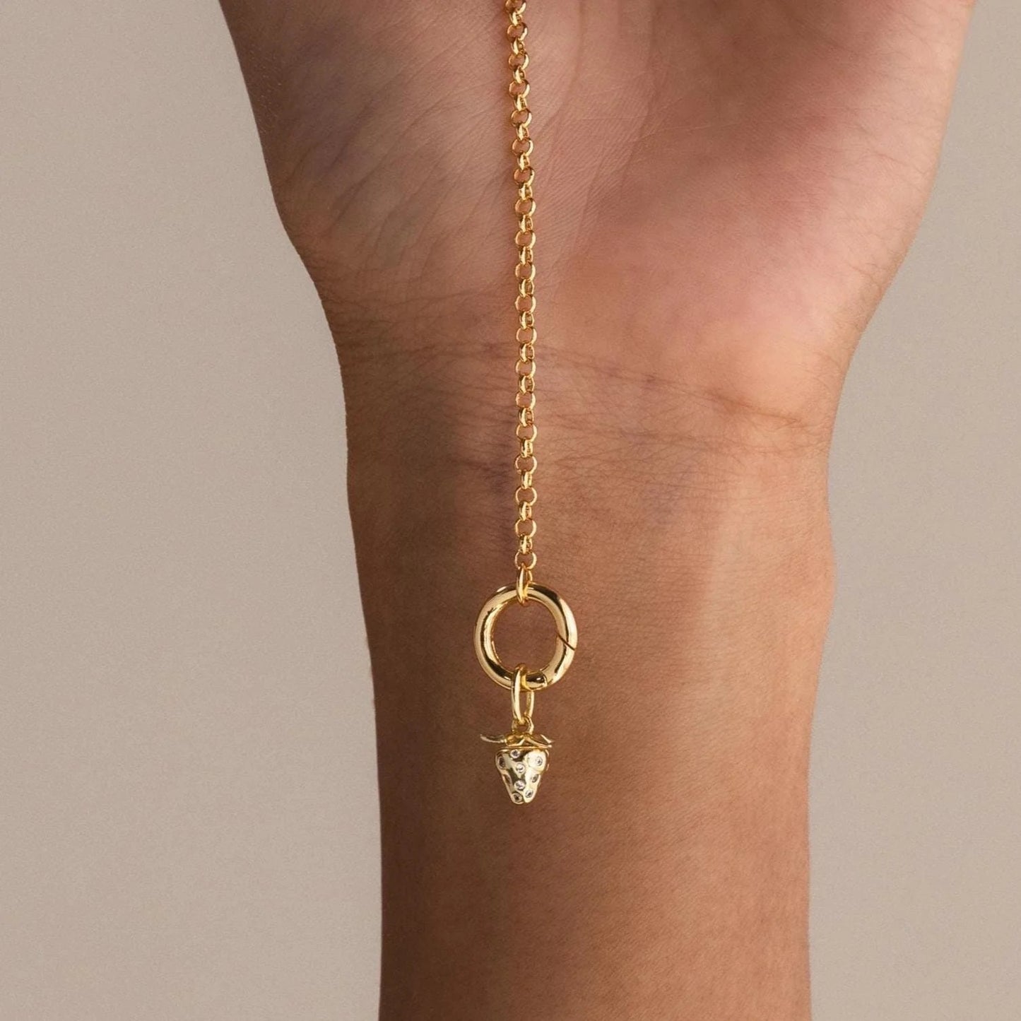 Gold chain with a lion head charm on a person's wrist against a neutral background