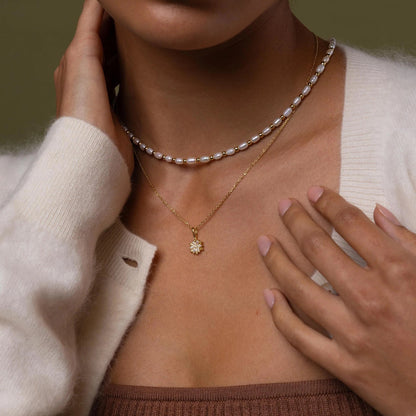 Woman wearing a pearl necklace and gold pendant against a brown background