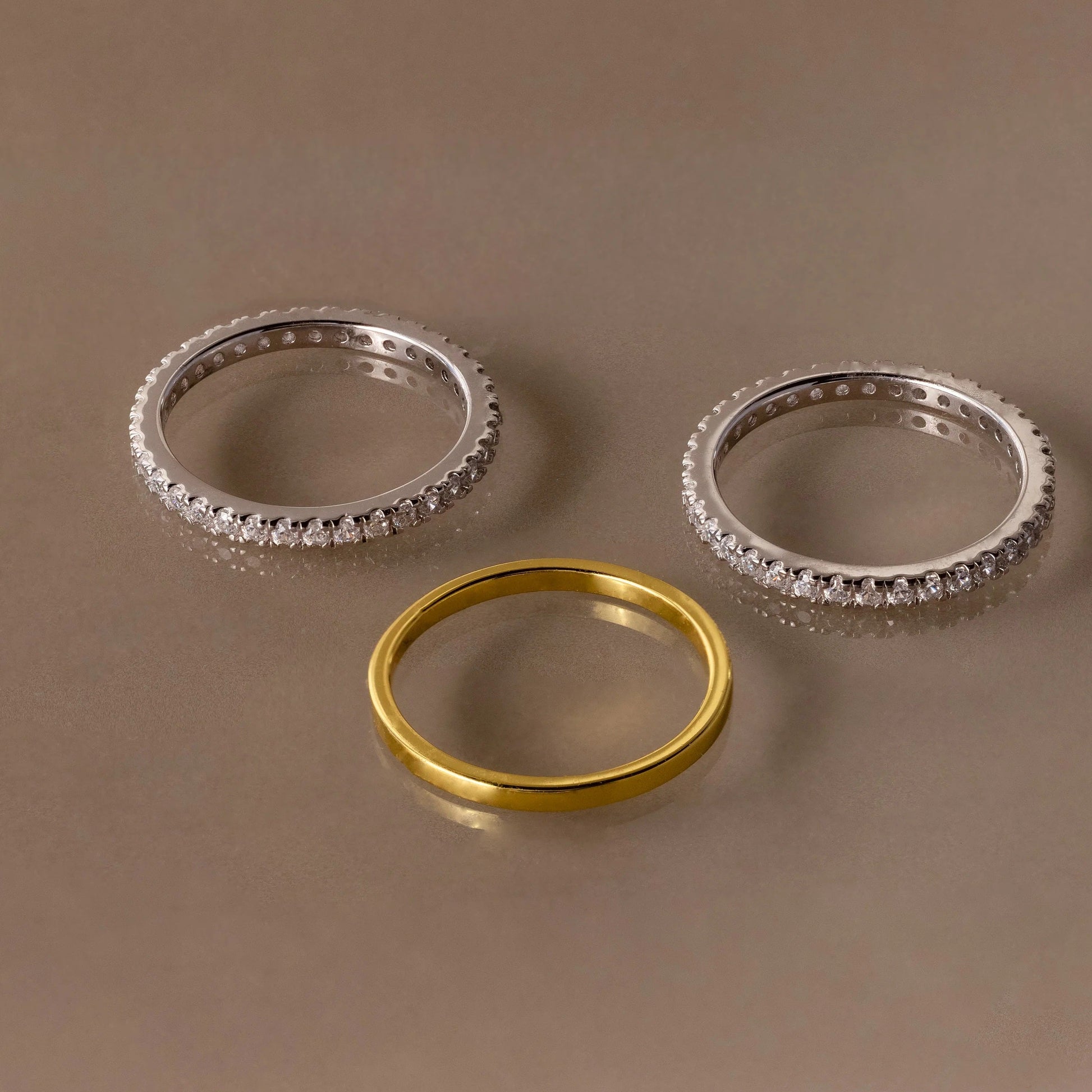 Three rings, two silver and one gold, on a brown background