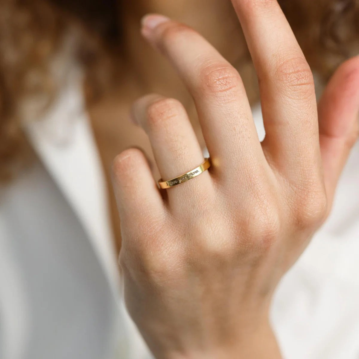 Close-up of a hand wearing a gold ring with engraved text, against a blurred background.