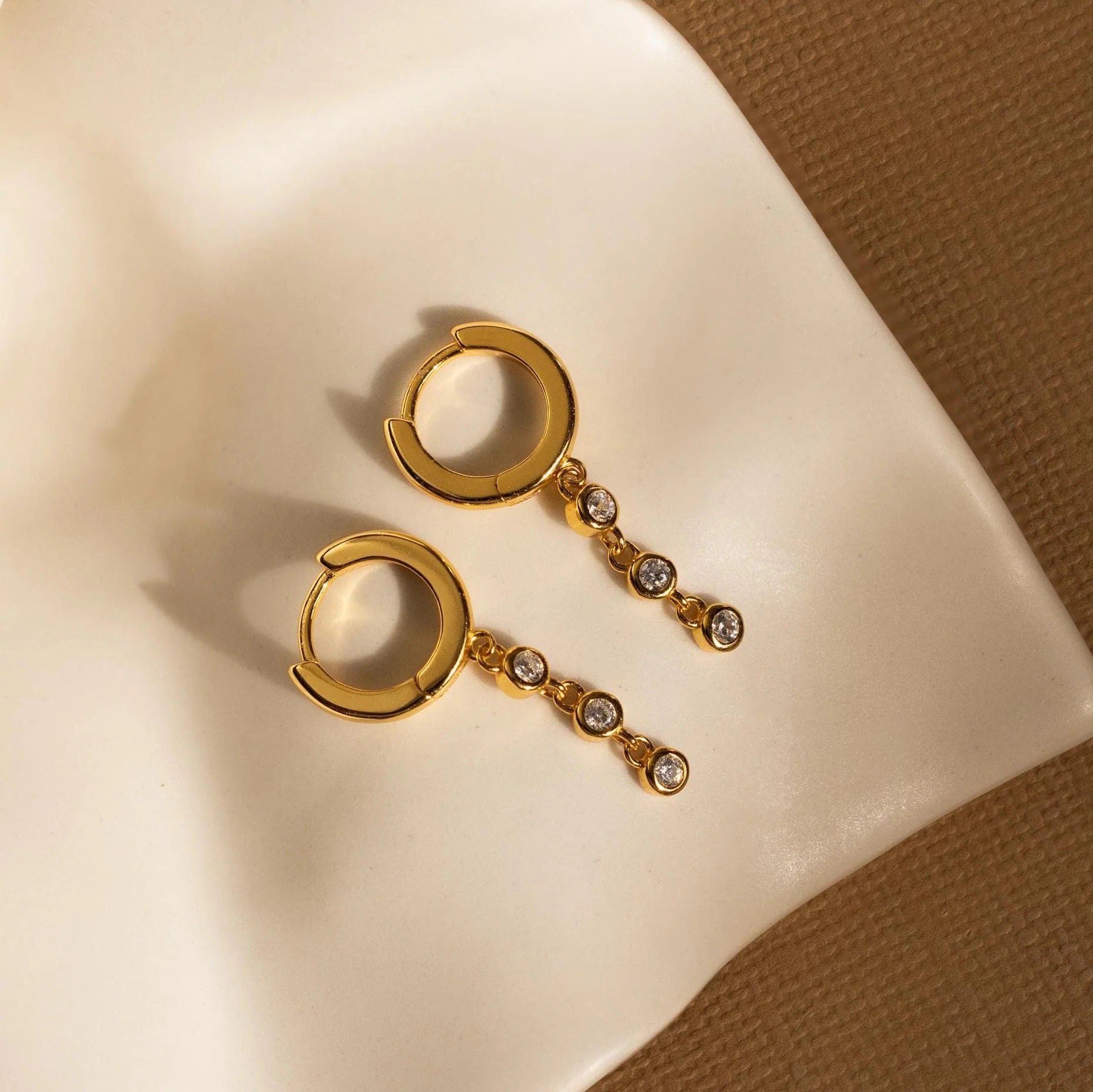 Gold hoop earrings with chain and stones on a beige surface