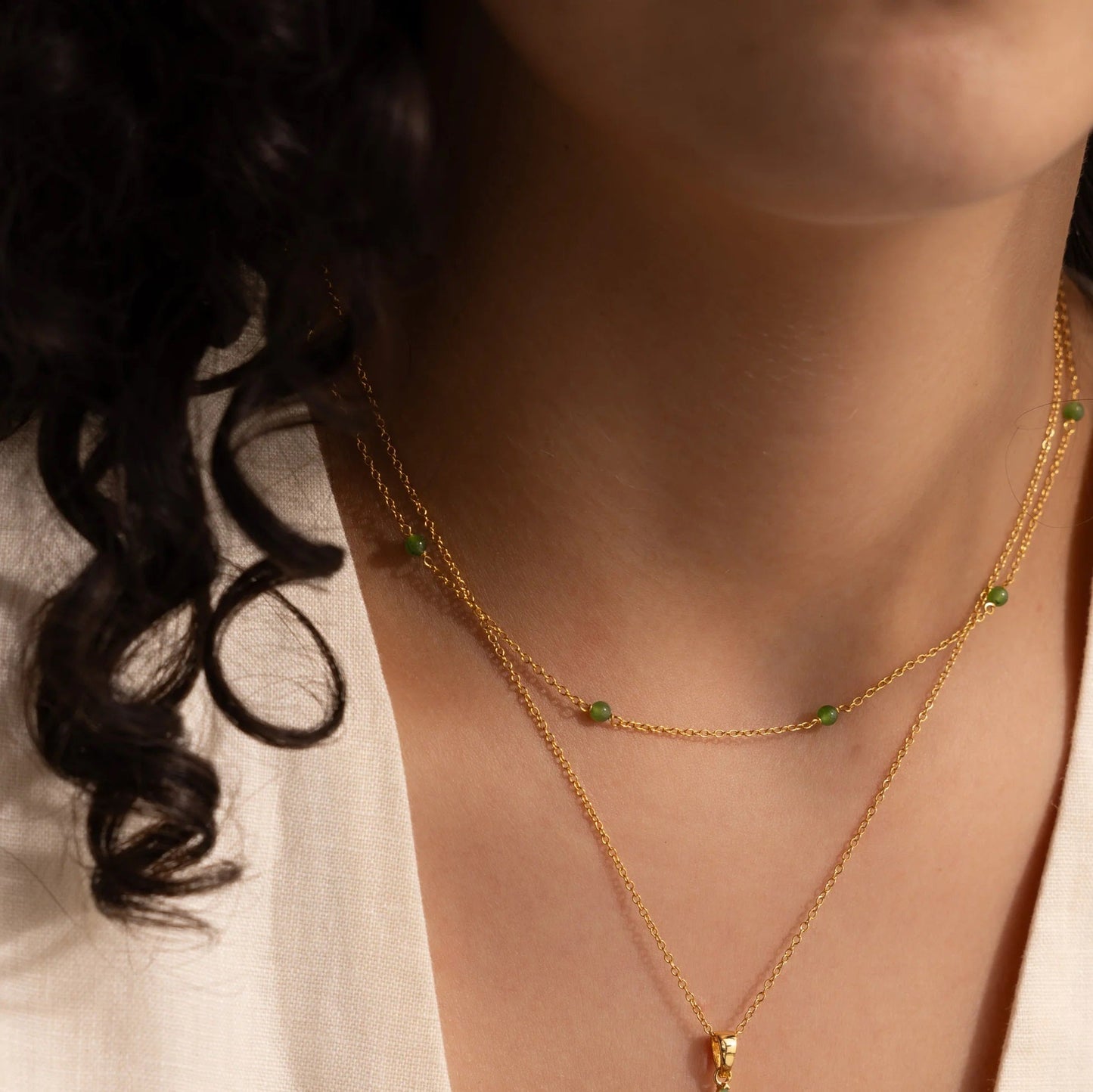 Woman wearing the Serenity Jade Cross Necklace, showcasing a radiant jade cross pendant layered with delicate gold chains.