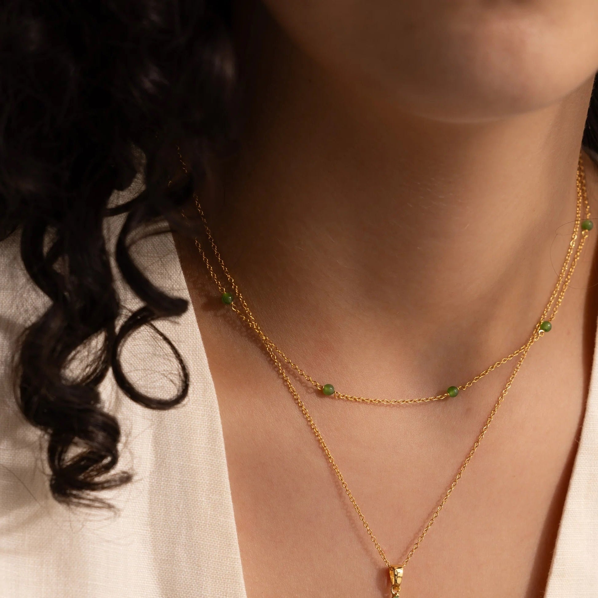 Woman wearing the Serenity Jade Cross Necklace, showcasing a radiant jade cross pendant layered with delicate gold chains.