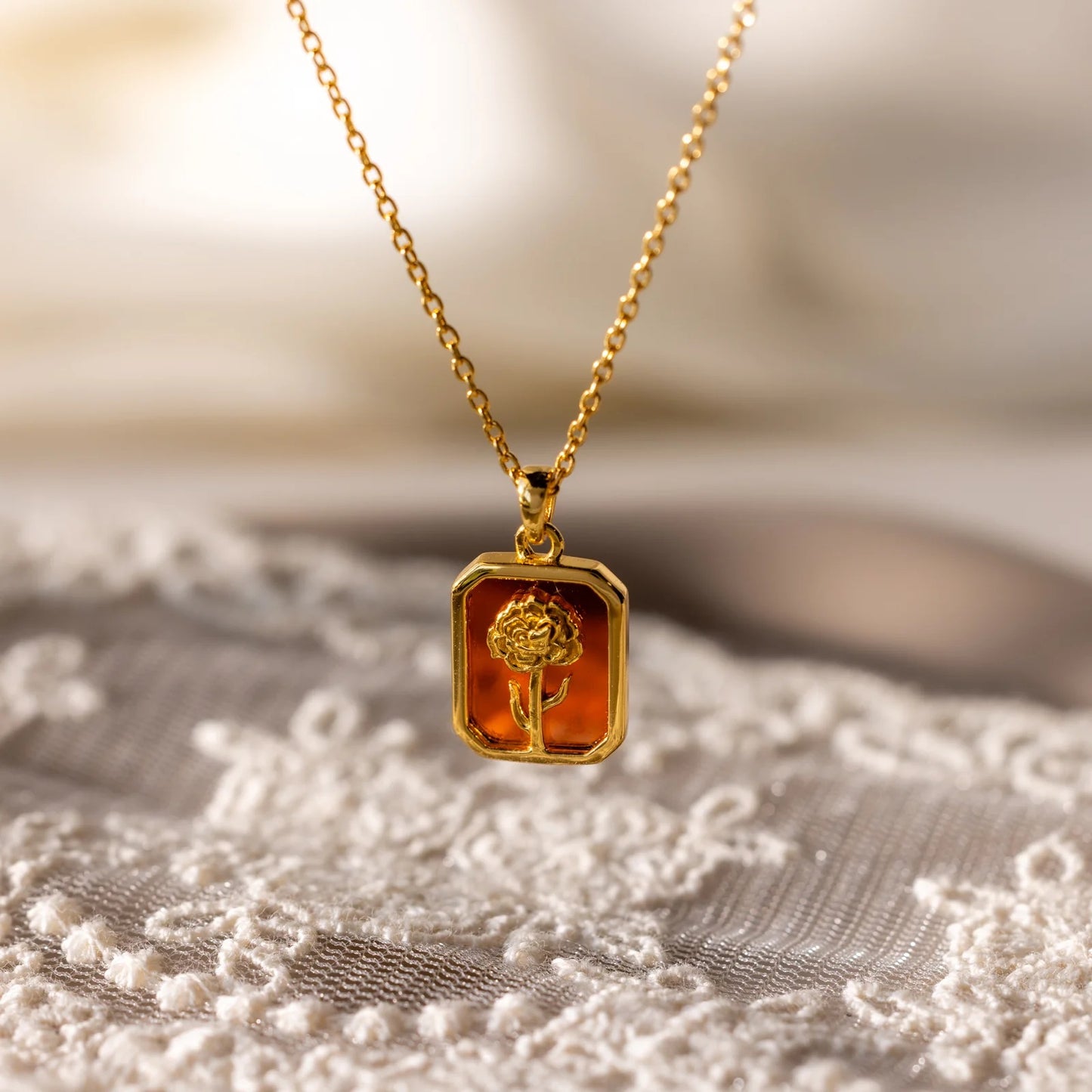 Gold necklace with a pendant featuring a rose design on a textured surface.