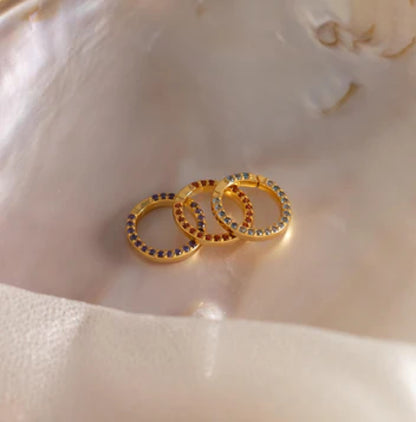 Gold hoop earrings with embedded stones on a shell background