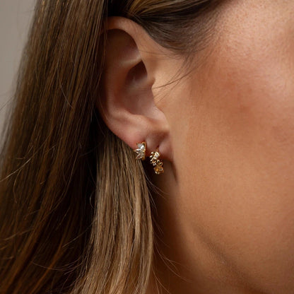 Close-up of a woman's ear wearing gold earrings with a neutral background
