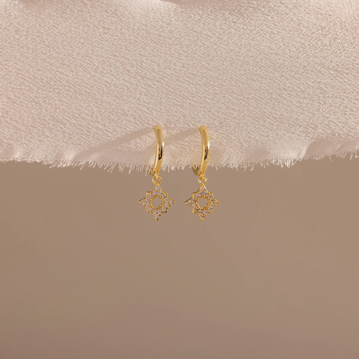 Gold earrings on a beige fabric background