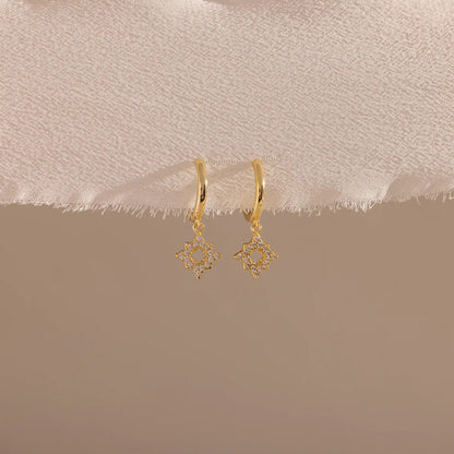 Gold earrings on a beige fabric background