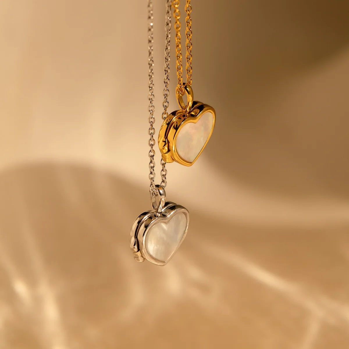 Two heart-shaped pendants on gold and silver chains against a beige background