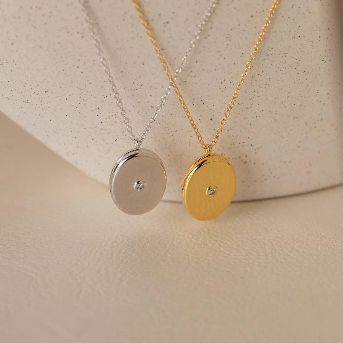 Two gold and silver necklaces with round pendants on a beige background
