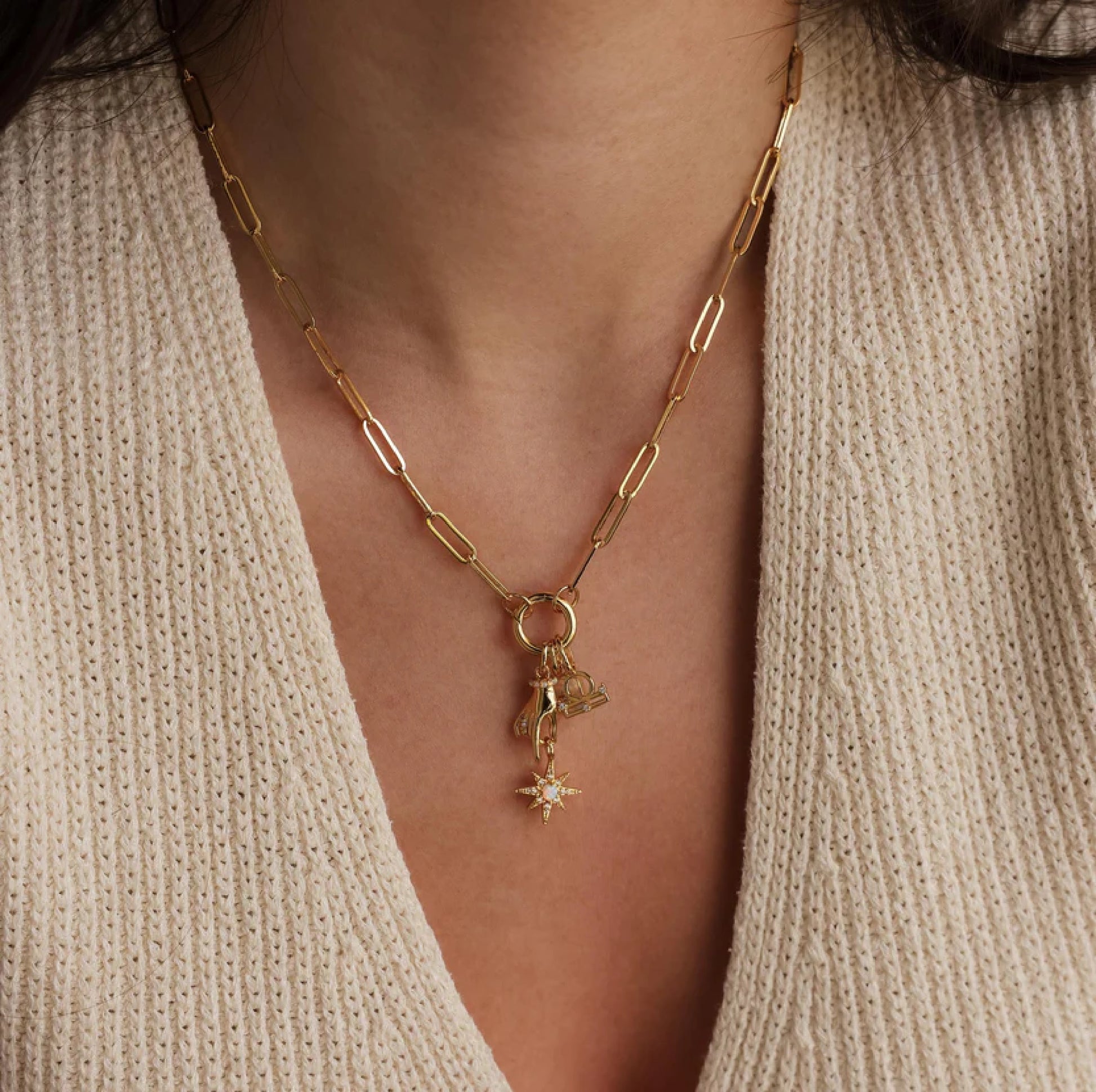 Gold necklace with a star pendant worn by a person in a beige sweater.