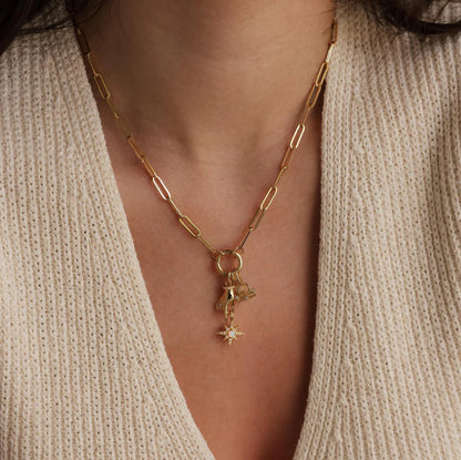 Gold necklace with a star pendant worn by a person in a beige sweater.