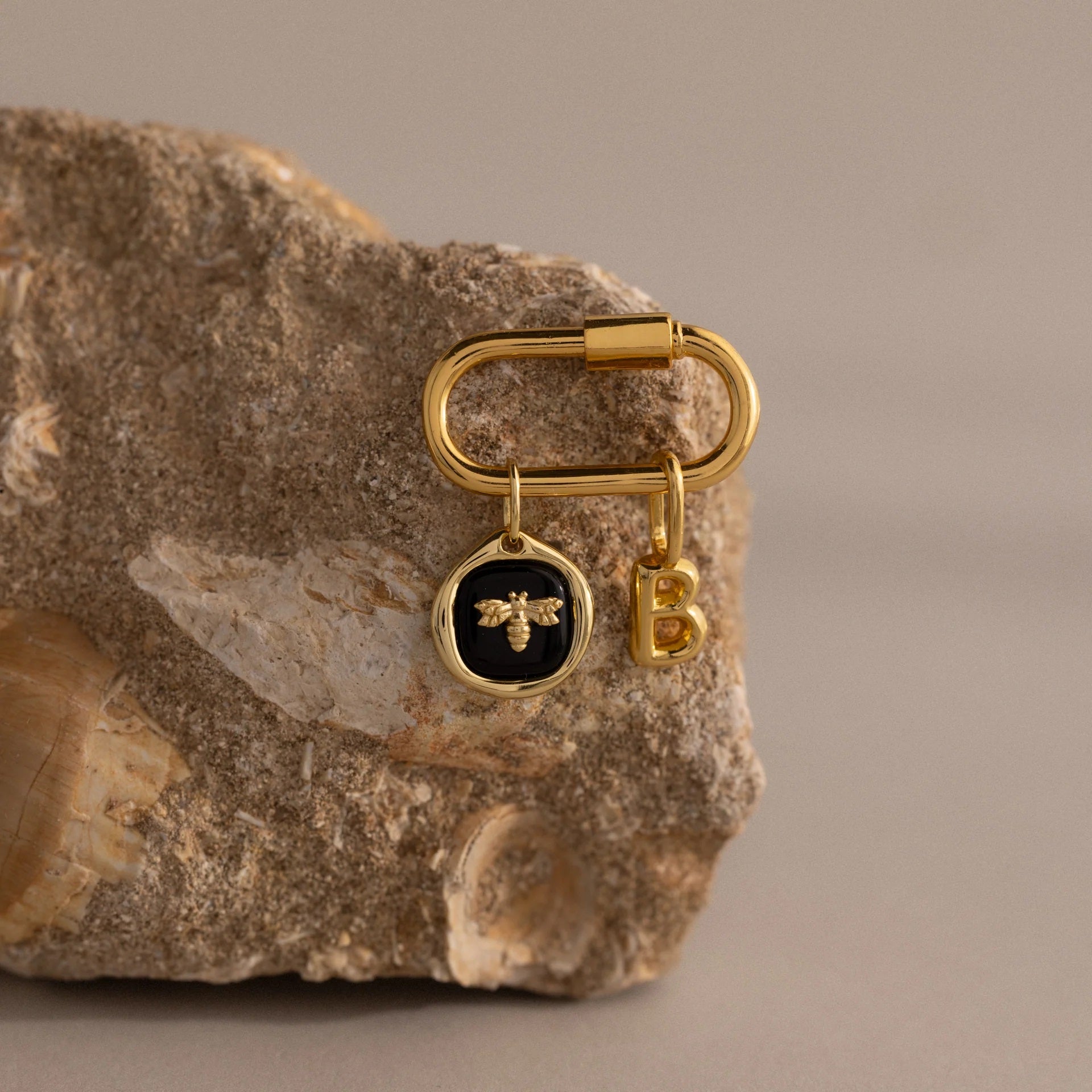 Gold keychain with bee charm and letter 'B' on a stone surface